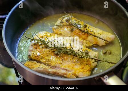 Fish fillet being fried in frying pan with rosemary and capers. Stock Photo