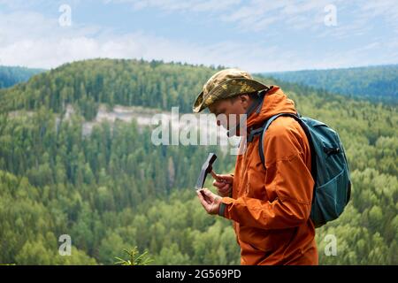 man geologist on an expedition examines a stone for hardness with a hammer Stock Photo