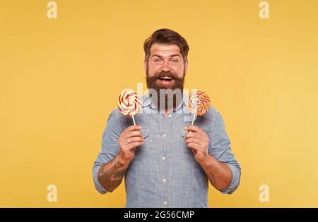 Happy bearded man hold tasty rainbow swirl candy pops great for birthday party and candy buffet yellow background, celebration Stock Photo