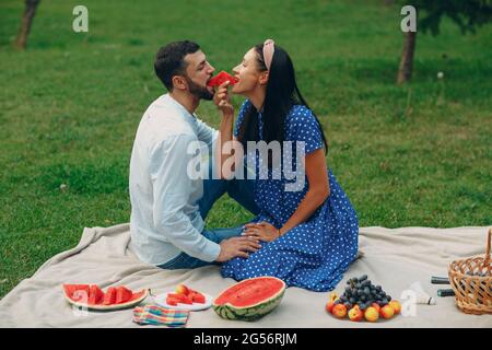 Young adult woman and man couple picnic at green grass meadow in park with fruits and basket Stock Photo