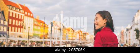 Happy Asian woman walking in Copenhagen city street. Denmark spring travel tourist visiting Nyhavn famous attraction, old water canal banner. Stock Photo