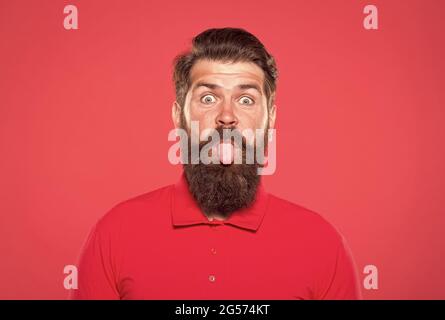 Pink tongue. Bearded and cheerful. Hipster appearance. Beard fashion. Barber concept. Man bearded hipster red background. Barber tips. Barbershop Stock Photo
