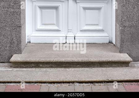 granite threshold at the entrance door made of white wood and gray facade cladding of an old retro building close-up front view, nobody. Stock Photo