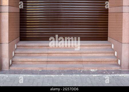 brown horizontal roller blinds closed entrance to the store with a facade facing granite stone close-up of the architecture of a building with steps, Stock Photo