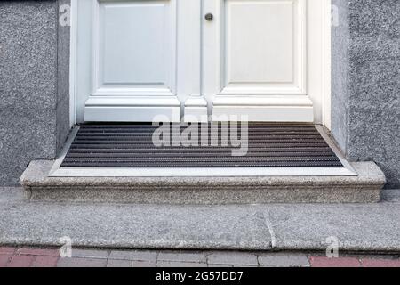 stone threshold with foot mat at the entrance door made of white wood and gray stone facade cladding of retro European architecture building close-up Stock Photo