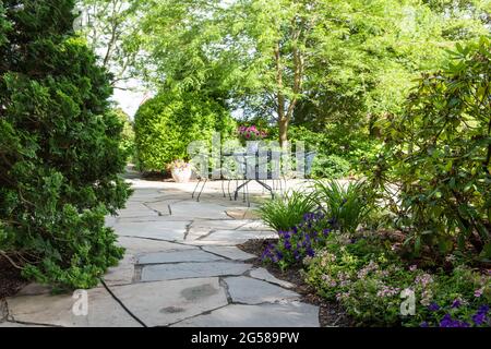 Stone patio with wrought iron furniture surrounded by lush landscaping. Stock Photo