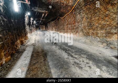 Underground mine. Underground road for transport. The walls and ceiling of the tunnel are reinforced with anchors and metal mesh Stock Photo