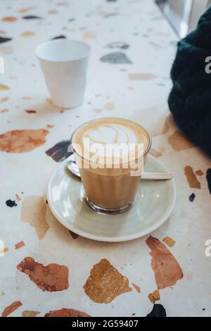 Latte with heart-shaped coffee art on a marble table in a cafe. Stock Photo