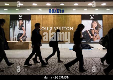 Commuters walking past homeless people sleeping outside the Odakyu luxury department store in Shinjuku, Tokyo, Japan Stock Photo