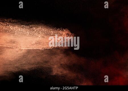 Launch brown particles exploding on black background. Brown dust splashing. Stock Photo