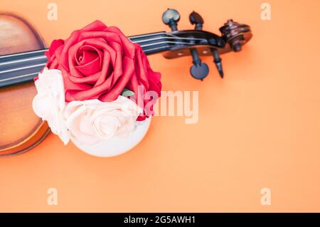 Vertical shot of roses and a violin on orange background with a copy space Stock Photo