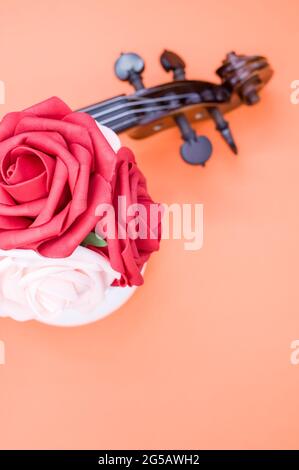 Vertical shot of roses and the pegbox of a violin on orange background with a copy space Stock Photo