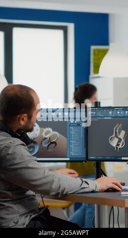 Diverse team of engineers working on computer at mechanical piece design cad sharing ideas about industrial project using dual displays setup. Black manager analysing 3D gears on CAD software. Stock Photo