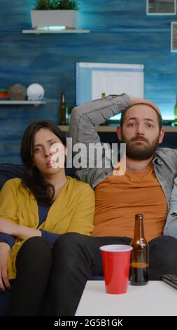 Multiethnic friends laughing while watching comedy movie enjoying time spend together. Excited mixed group of people eating snacks, drinking beer having fun late at night during relaxed party Stock Photo