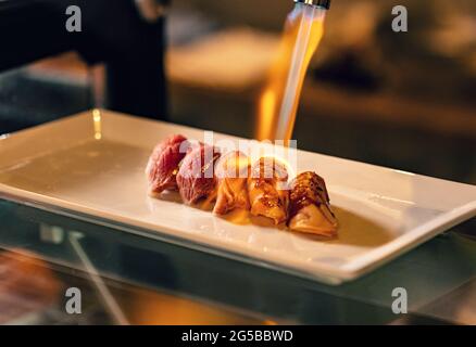 Close up hand of chef using kitchen torch burn on salmon sushi, japanese cuisine. Stock Photo