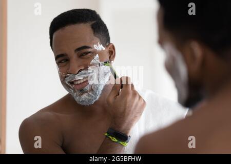 Happy handsome mixed race African man shaving with razor Stock Photo