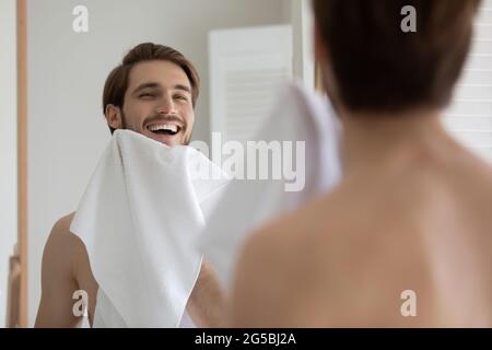 Happy attractive young millennial guy drying beard with white towel Stock Photo
