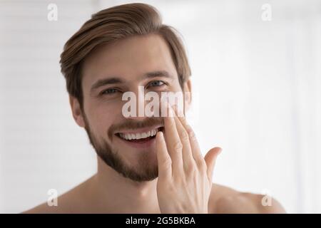Head shot of young attractive guy applying moisturizer Stock Photo