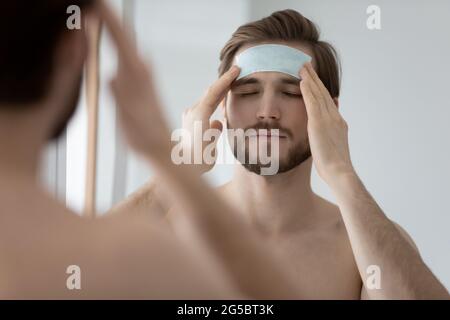 Calm metrosexual millennial man applying cleansing patch on forehead Stock Photo