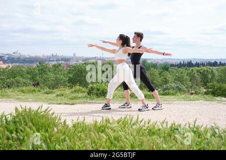 Young couple doing warrior two yoga pose in a park. Fitness outside. Stock Photo