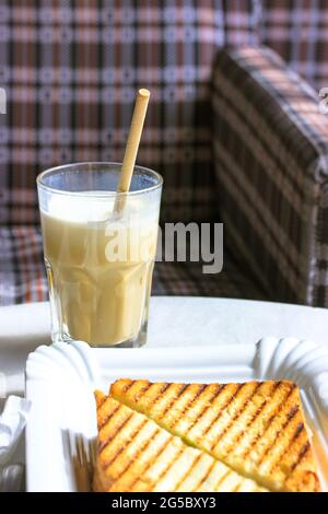 A glass of coffee drink frappe, cappuccino, latte with an eco-friendly paper tube and two grilled sandwiches on a beautiful white plate against a chec Stock Photo