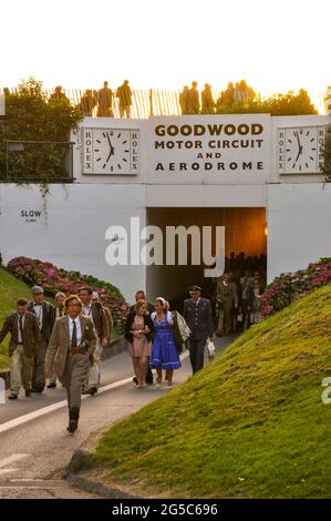 Visitors in period costumes beginning to leave the Goodwood Revival after the last motor races of the day. Sun setting behind the pedestrian tunnel Stock Photo