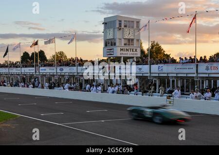 Historic motor racing into the evening with a classic car racing at the Goodwood Revival 2012 passing the pit area at sunset. Recreating endurance Stock Photo