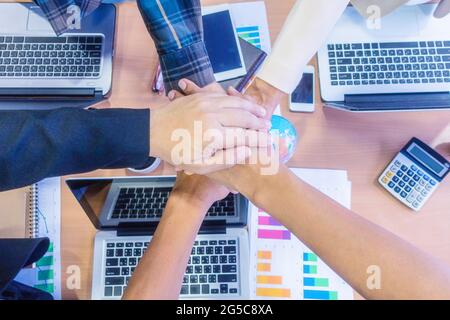 Business people stacking hands close up, office desktop on background, concept of teamwork. Stock Photo