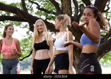 black african american woman feel boring in talking with young multiethnic women friends group on yoga exercise class in the park at weekend morning. Stock Photo