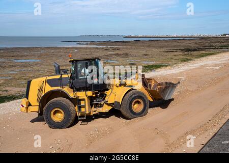 A construction excavator prepares a beach in Brittany for the arrival of tourists Stock Photo