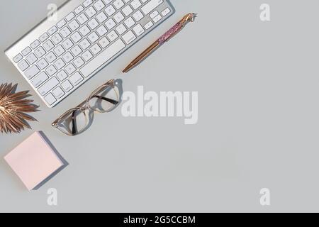 Overhead shot of business desktop with keyboard, glasses, pen on gray background with copy space Stock Photo