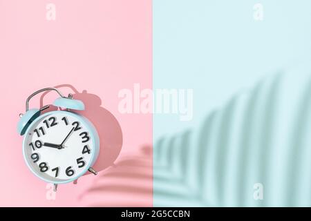 Old fashion blue alarm clock on pink and blue background, flat lay with copy space and palm shadow Stock Photo