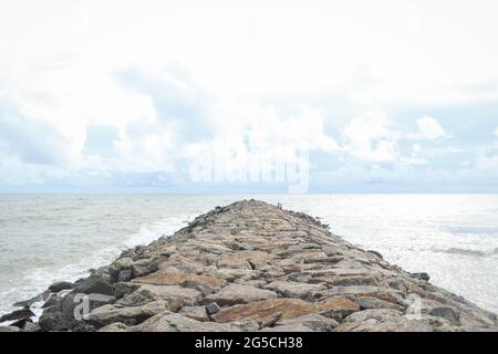 cloudy sky and a man made rocky path made with large stones on the beach Stock Photo
