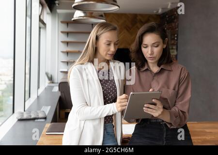 Focused two female colleagues working using digital tablet. Stock Photo