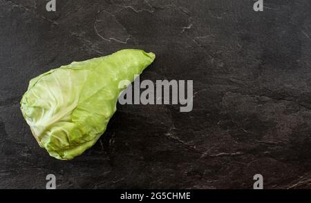 White pointed cabbage - also known as sweetheart hispi with few water drops on leaves - black table with slate like structure, under view from above, Stock Photo