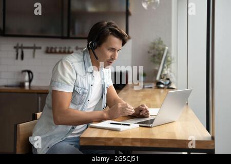 Focused young man in wireless headset holding video call. Stock Photo