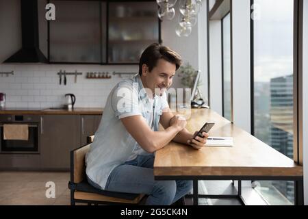 Happy young handsome man using smartphone in office kitchen. Stock Photo