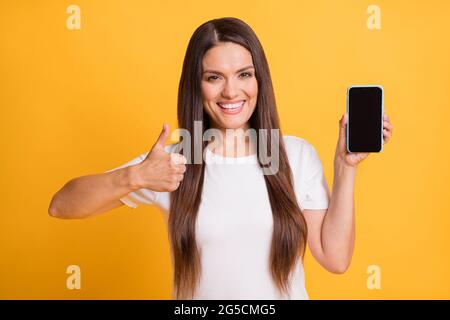 Photo portrait of woman showing mobile phone screen with empty space like gesture smiling isolated on vibrant yellow color background Stock Photo