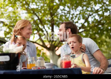 mother and father with their children in laps sitting outdoor in nature, looking each other, smiling Stock Photo