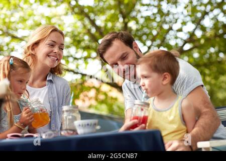 cheerful caucasian family sitting outdoor, drinking juices, enjoying. father helping his son to drink juice on straw. Stock Photo