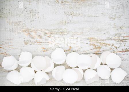 Lots of broken white eggshells on a light wooden background. Copy space. Stock Photo