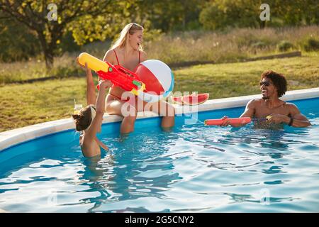 multiethnic group of young people having fun in swimming pool, playing with water guns and inflatable ball Stock Photo