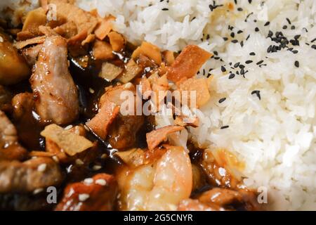 Close-up of Vietnamese food: rice sprinkled with black sesame seeds, beef in gravy, fried carrots. Stock Photo