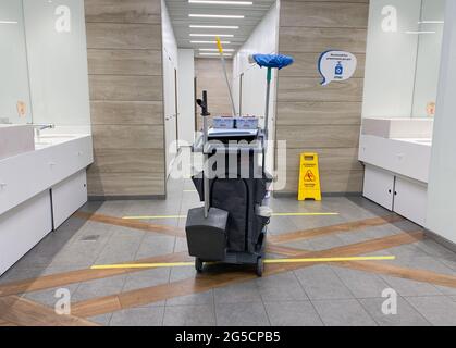 MOSCOW, Russia, May 2021: A cleaning cart with mops in an empty public toilet. On the floor dividing lines for social distance, yellow warning sign we