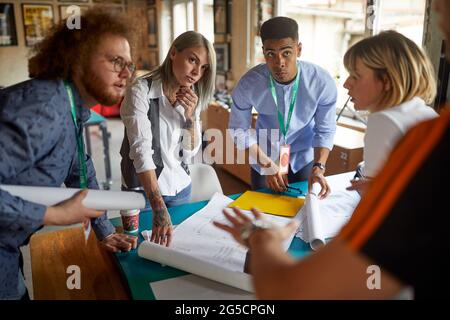 A group of young creative colleagues in a working atmosphere in the office is discussing about project they are working together on Stock Photo