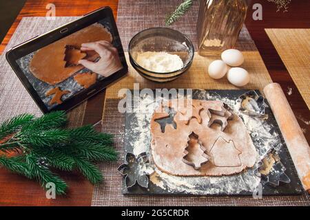 Following the recipe on a digital tablet - cutting out of the dough using a mold for making Christmas gingerbread. Stock Photo
