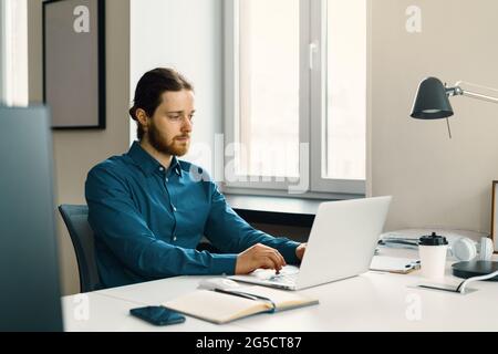 Young focused man freelancer working on laptop computer remotely Stock Photo