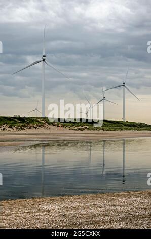 Large windturbines on Maasvlakte peninsula near Rotterdam, The Netherlands, reflecting in a shallow puddle on the beach under a dramatic sky Stock Photo