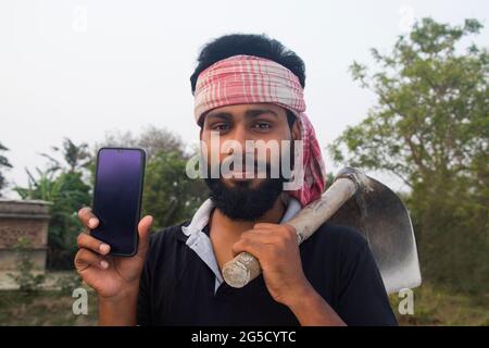Young Indian Rural farmer Showing on mobile phone in agricultural field Stock Photo