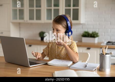 Interested cute little kid girl studying remotely. Stock Photo